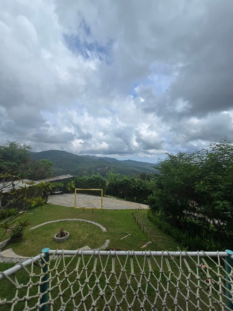 Rope-net deck overlooking the lawn, fire pit, and rolling green mountains at Panuluyan Farmstay