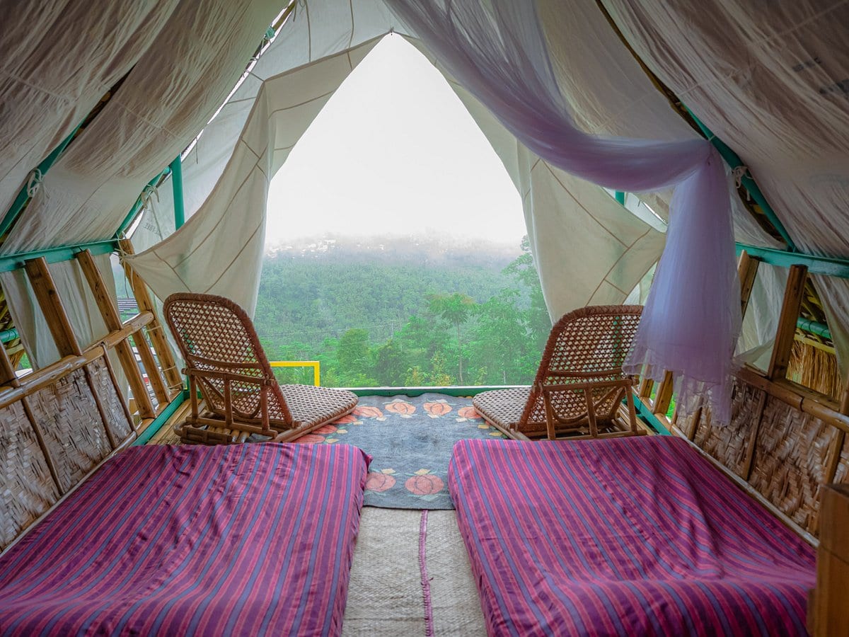 Glamping tent interior at Panuluyan Farmstay — twin beds, rattan chairs, and a mountain view through draped canvas