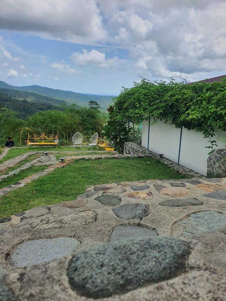 Stone-paved garden patio with yellow wrought-iron seating and a mountain valley view at Panuluyan Farmstay