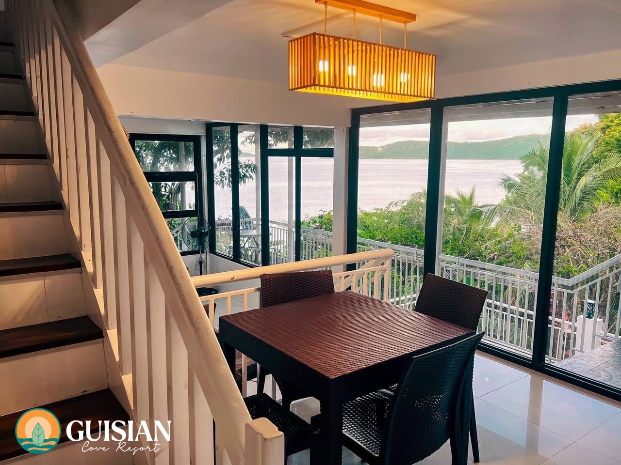 Villa interior at Guisian Cove Resort — wooden dining table and chairs beside floor-to-ceiling windows opening to the cove