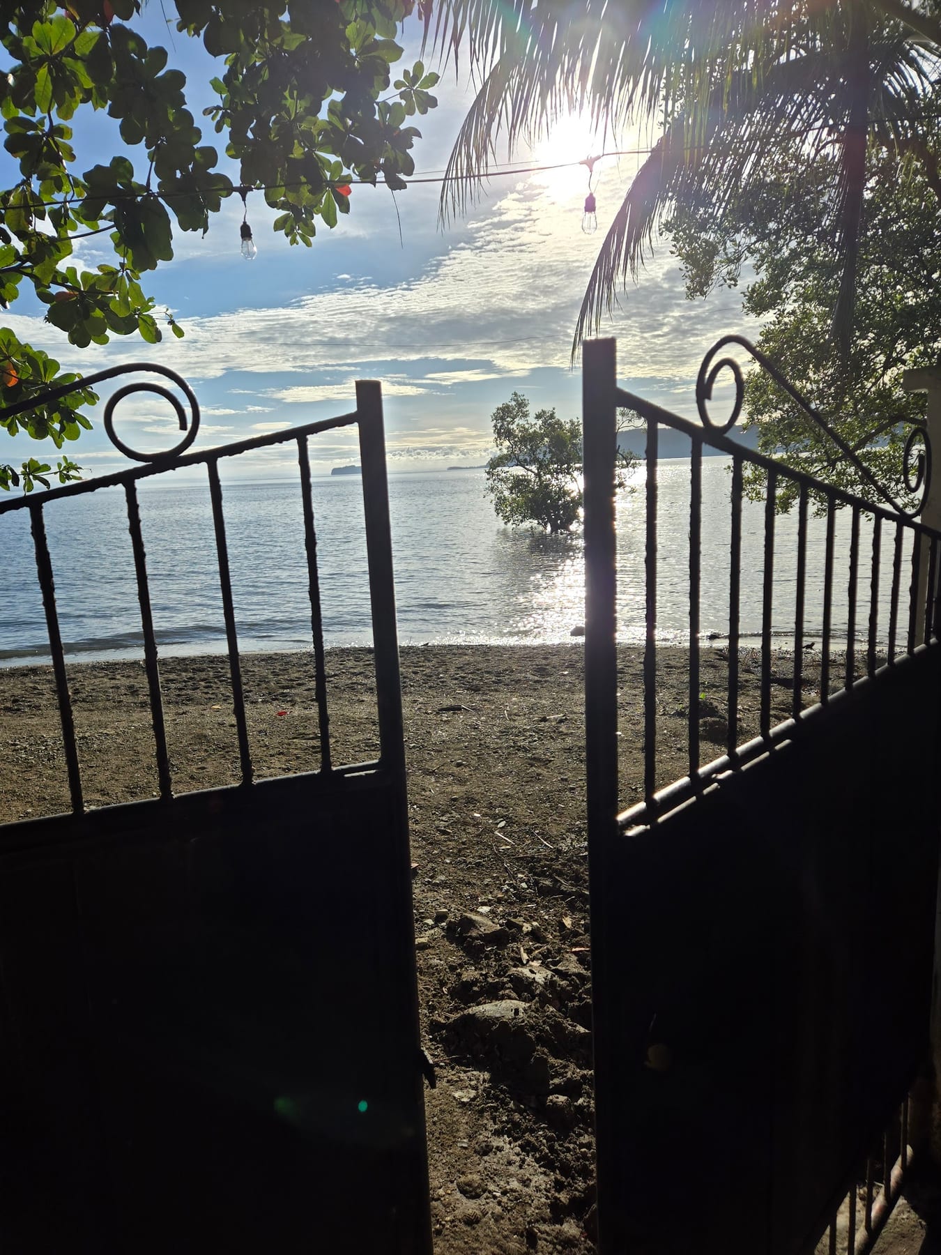 Wrought-iron beach gate at Guisian Cove Resort framing the cove, with hanging lights and palm fronds