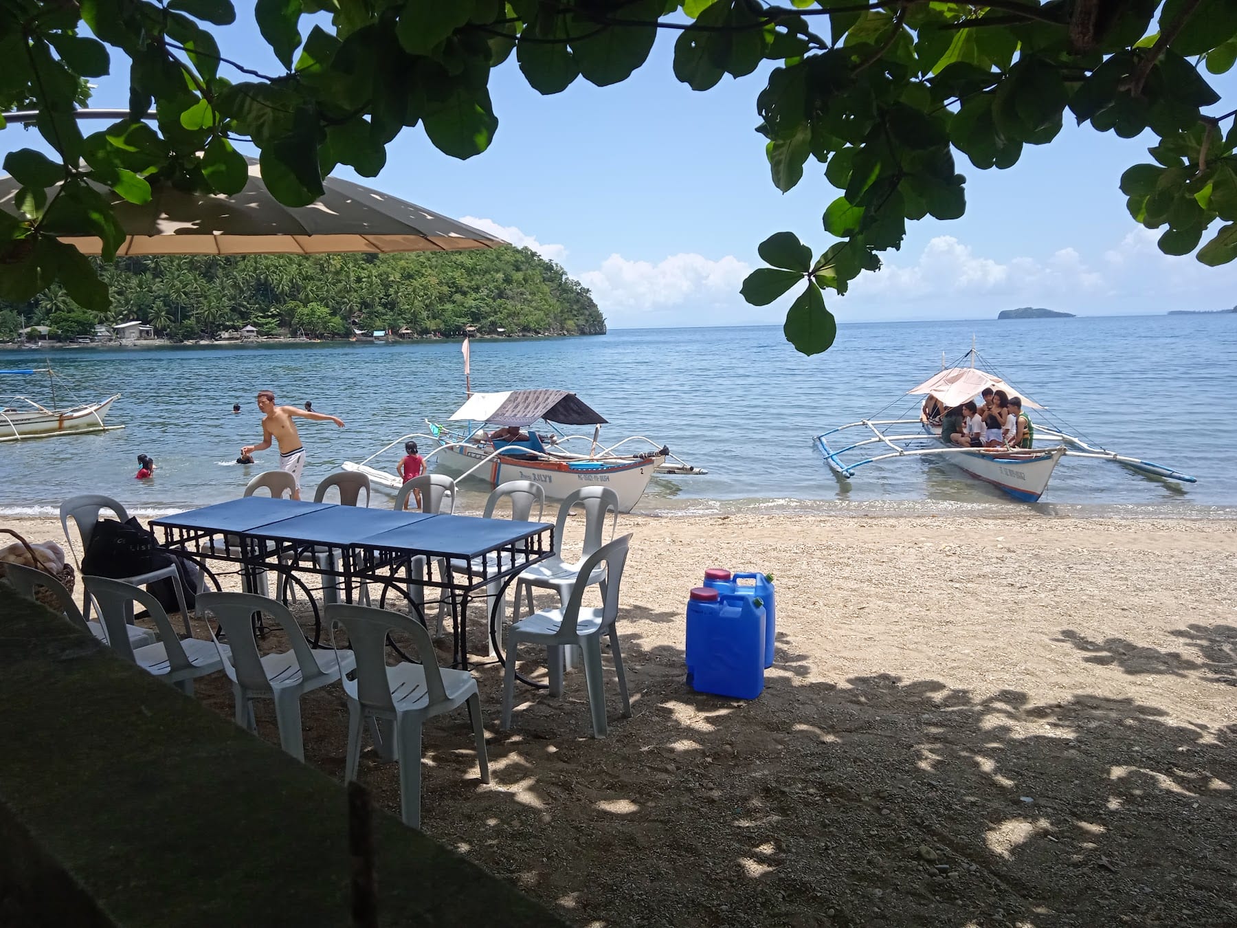 Beach-level dining tables on the sand at Guisian Cove Resort, with outrigger boats moored just offshore