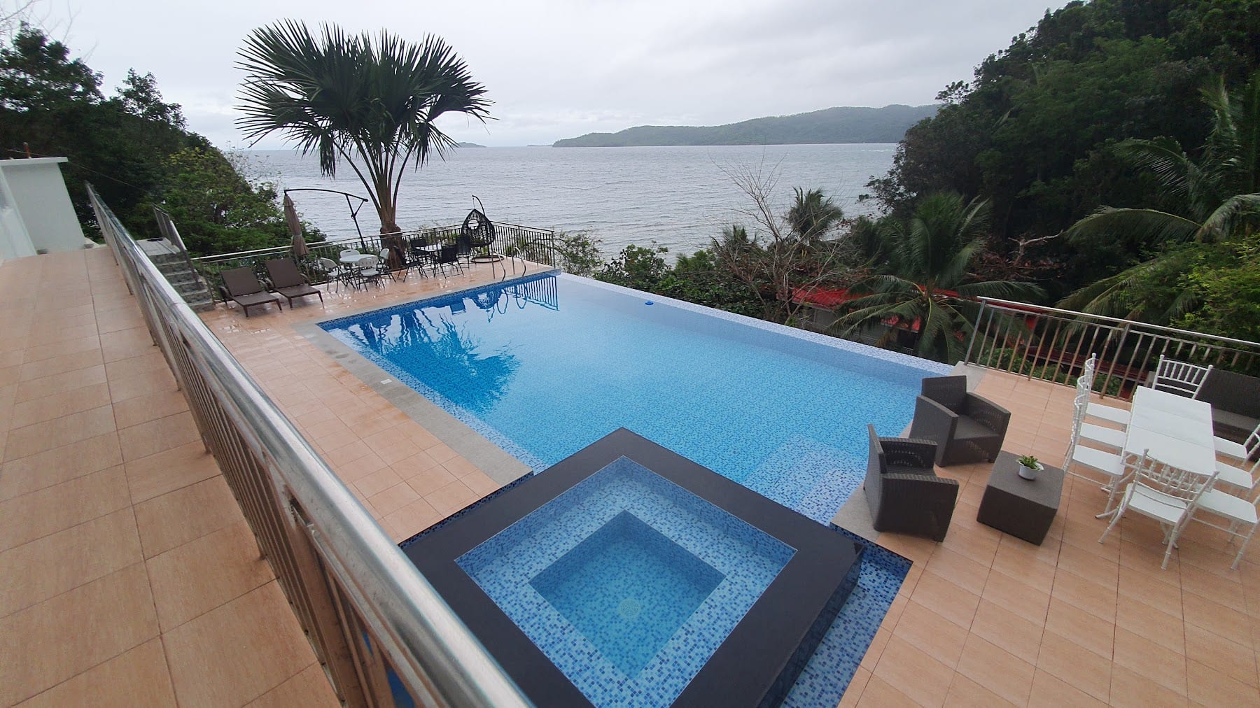 Infinity pool and inset jacuzzi at Guisian Cove Resort, with palm tree, lounge chairs, and a wide cove view
