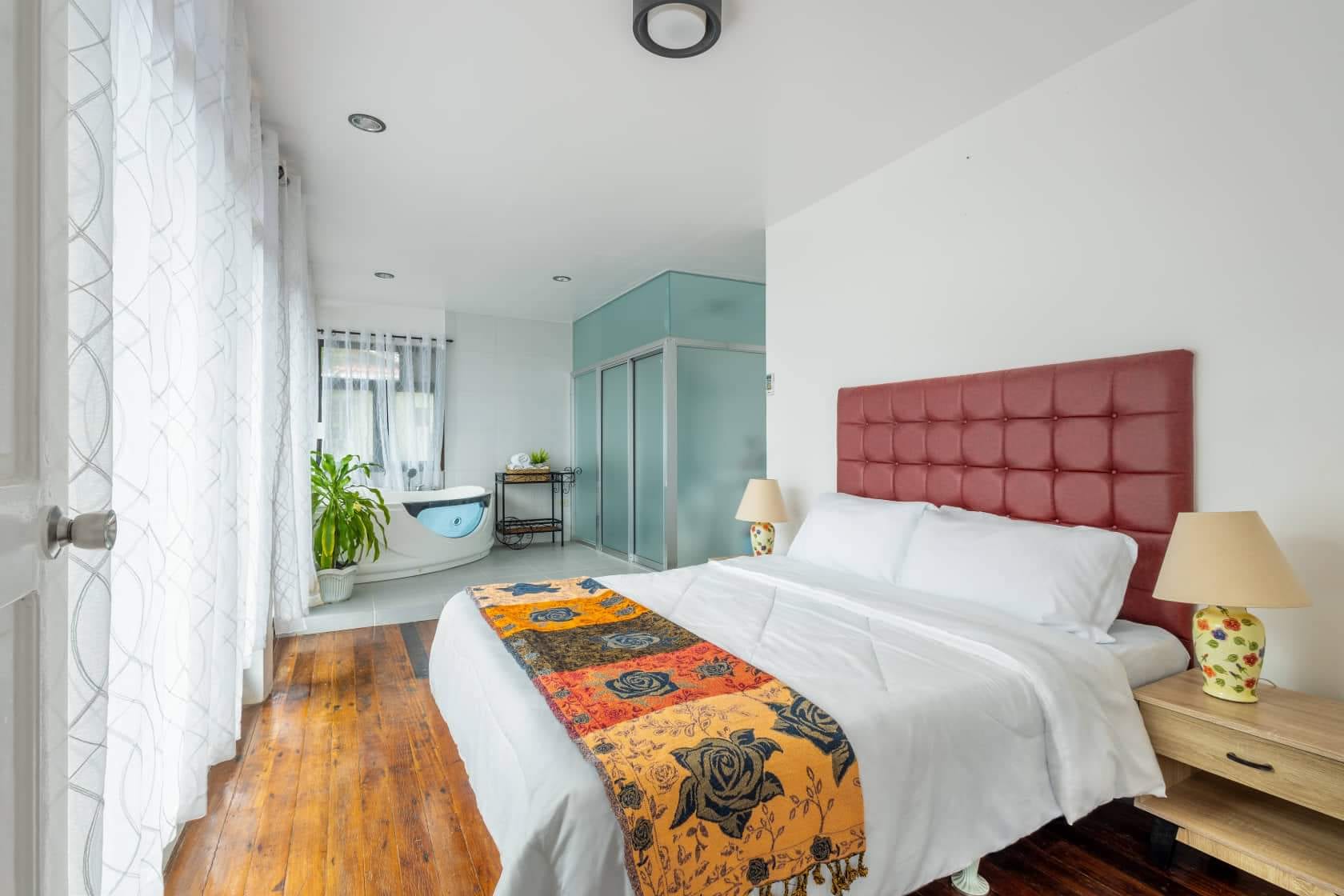 Bedroom interior at Guisian Cove Resort with king bed, red-tufted headboard, and a soaking tub by the curtained window