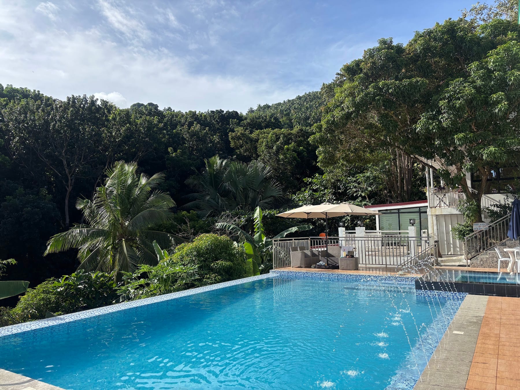 Outdoor pool with water-feature spillway, parasol seating, and the lush green hillside at Guisian Cove Resort