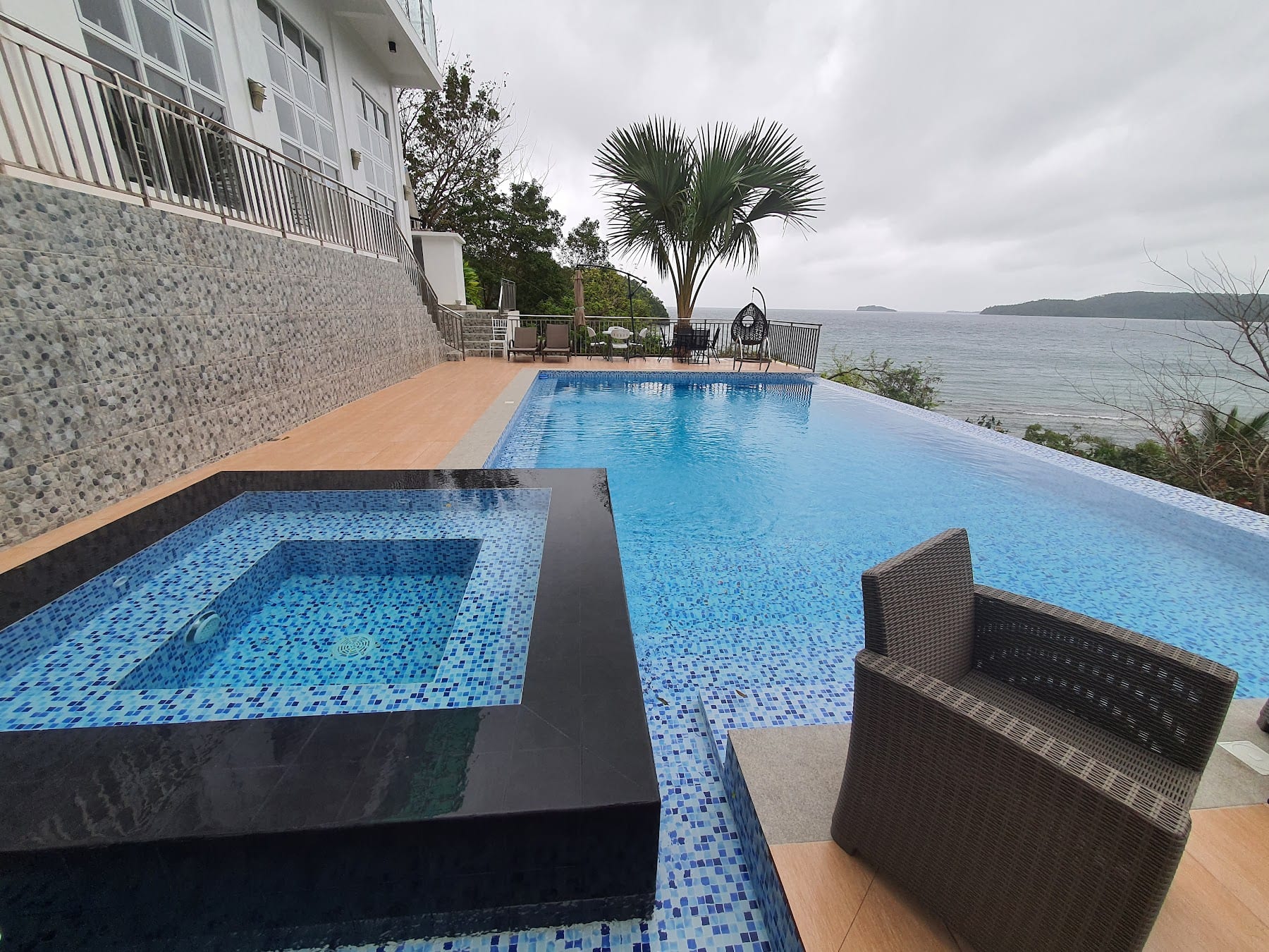 Pool deck closeup at Guisian Cove Resort showing the inset jacuzzi, infinity edge, palm tree, and a peek of the cove