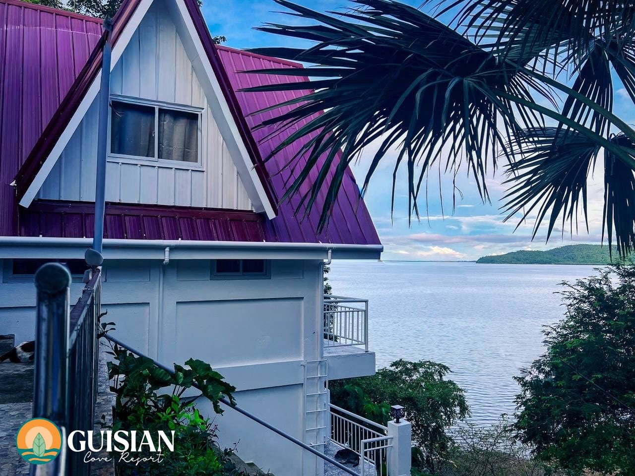 A-frame cabin with magenta roof above the cove at sunset, Guisian Cove Resort