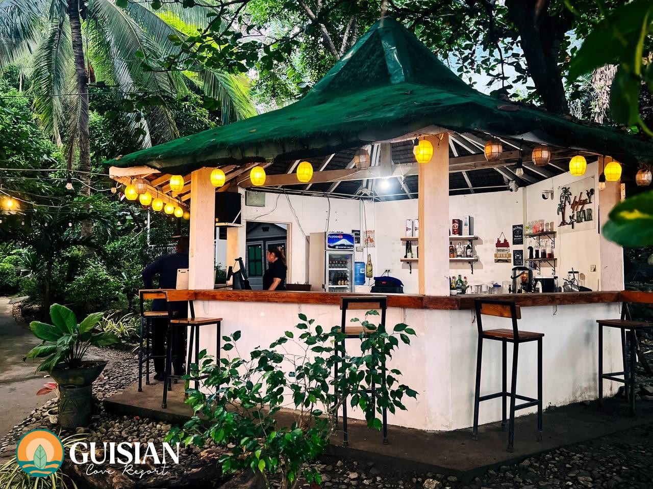 Open-air bar pavilion lit by hanging yellow lanterns at dusk, Guisian Cove Resort